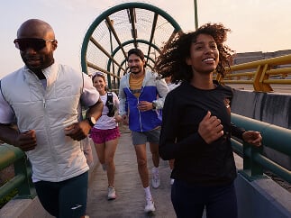 Four people smiling and running on a sidewalk