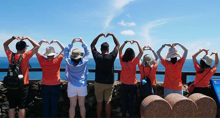 A group of people face a body of water on a sunny day