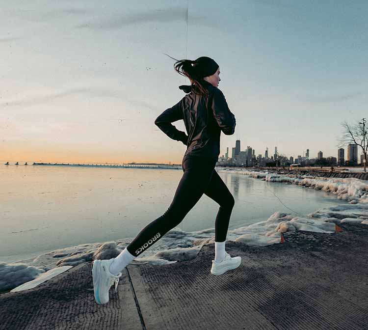 Woman running on a snow-lined sidewalk, with a city skyline in the background