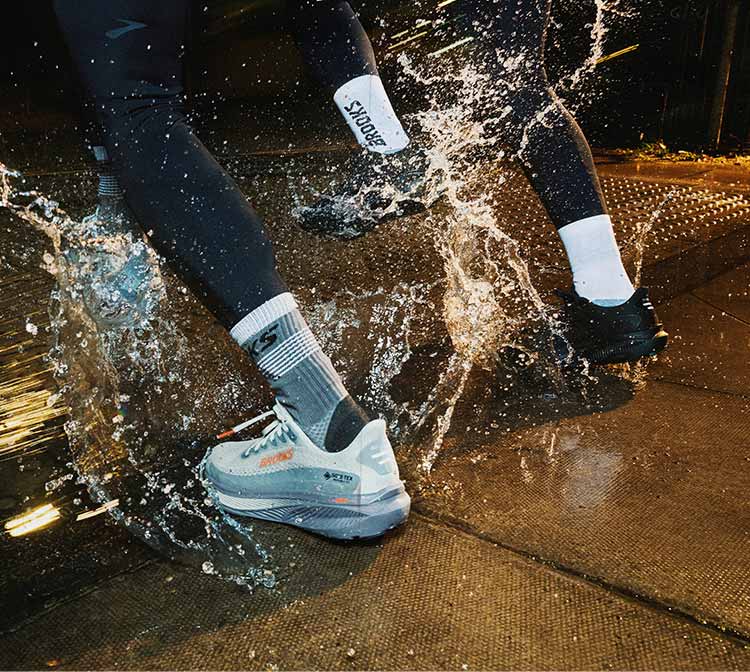 A person in Brooks shoes splashes water while running on a sidewalk
