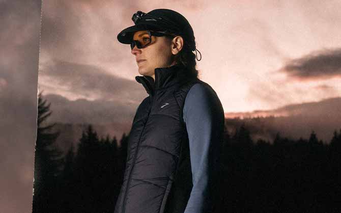 Woman wearing Brooks apparel looks to the side, against a pink sunset