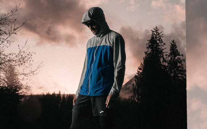 Man wearing Brooks apparel looks to the side, against a pink sunset