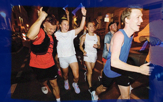 A group of runners smiling and running down a street, hands in the air