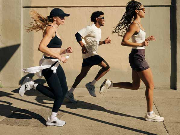 Three people wearing Brooks gear run on a sunny sidewalk