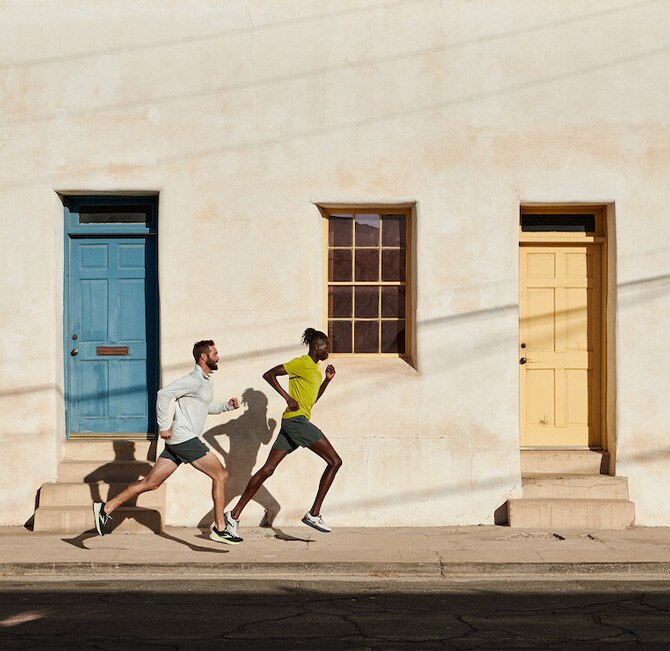 Two men running on sidewalk in front of building with coloured doors