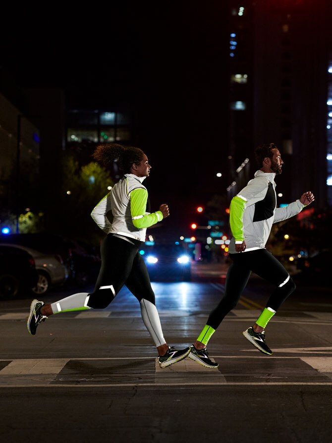 Side view of a runner crossing a street at night while wearing the Run Visible collection